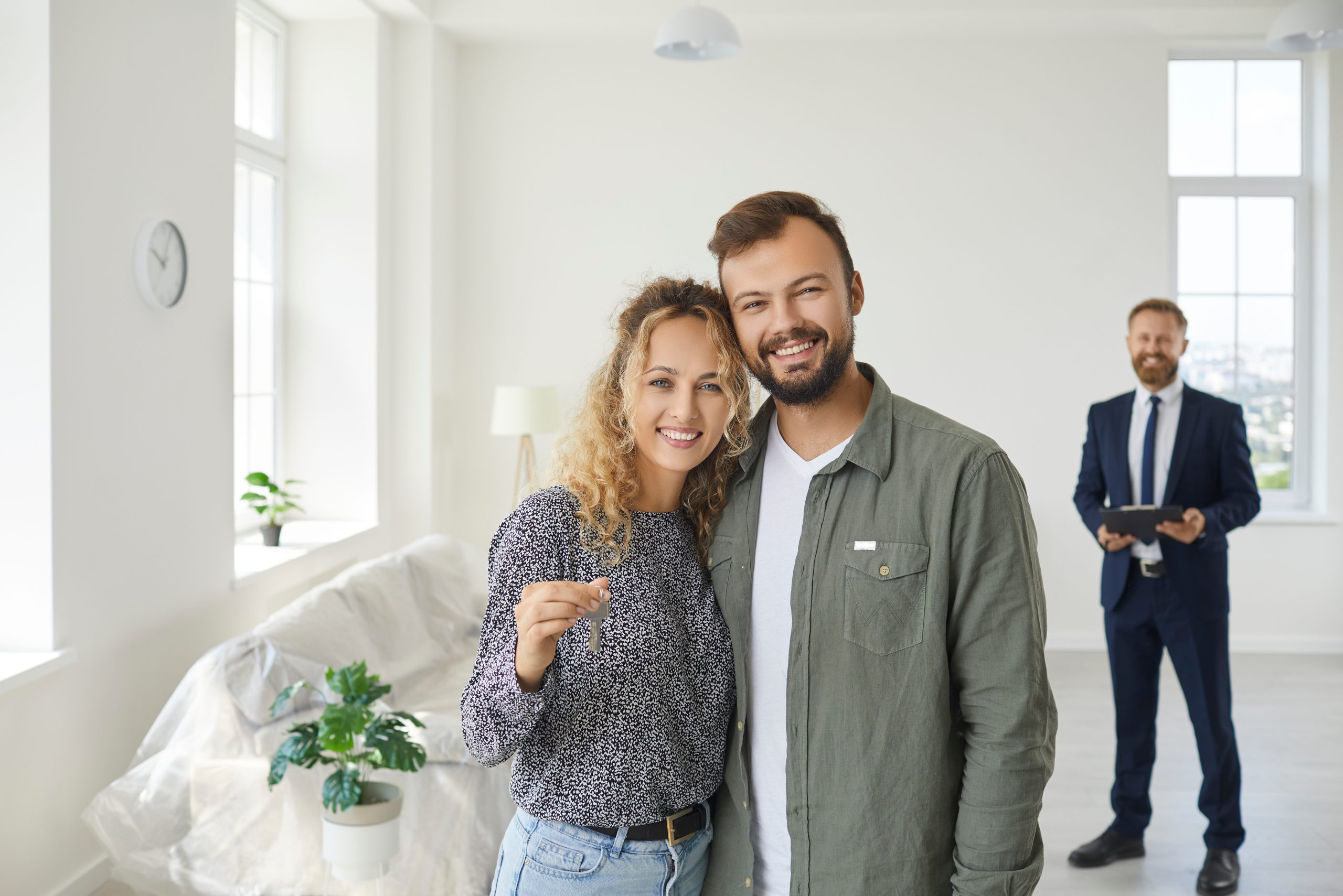 Happy young couple standing in their newly bought house, smiling and showing the keys