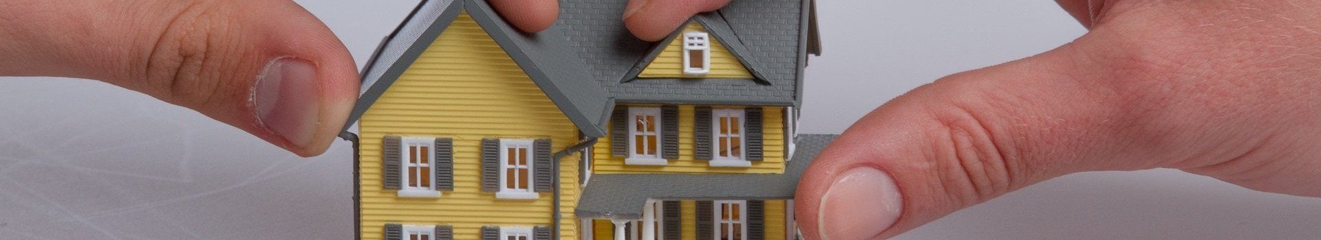 Zwei Hände greifen nach gelben Modellhaus