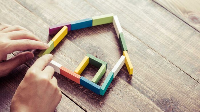 Person legt mit Holklötzchen ein Haus zusammen als Symbol für die geerbte Immobilie