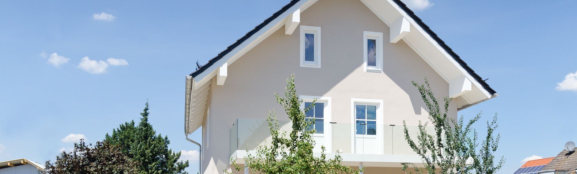 Giebelansicht eines Einfamilienhauses mit sehr heller Fassade und Sträuchern davor