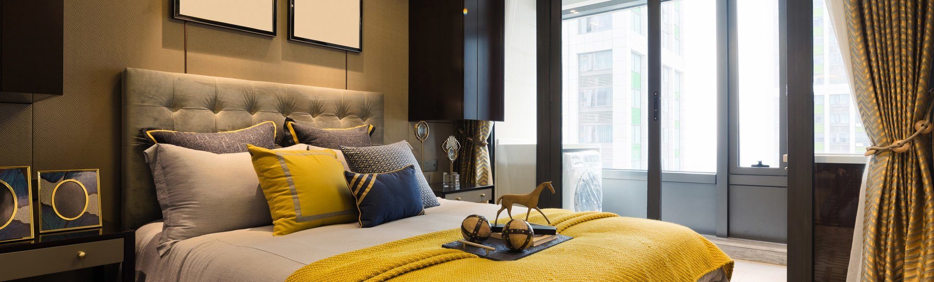 interior of modern bedroom Hotelzimmer mit einem grauen Boxspringbett und einer gelben Tagesdecke und gelben Dekoelementen