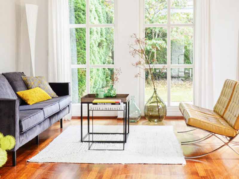 Helles Wohnzimmer mit anthrazit farbener Couch mit gelben Dekokissen und hellem Teppich