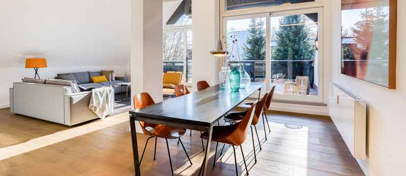 Moderner, heller Wohnraum mit heller Couch und dunklem Esstisch, mit braunen Stühlen drum