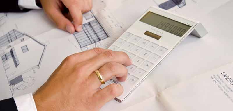Aignerimmobilien_fakten_800x384px Männerhand mit goldenem Ehering, die auf einem Taschenrechner von Aigner Immobilien tippt