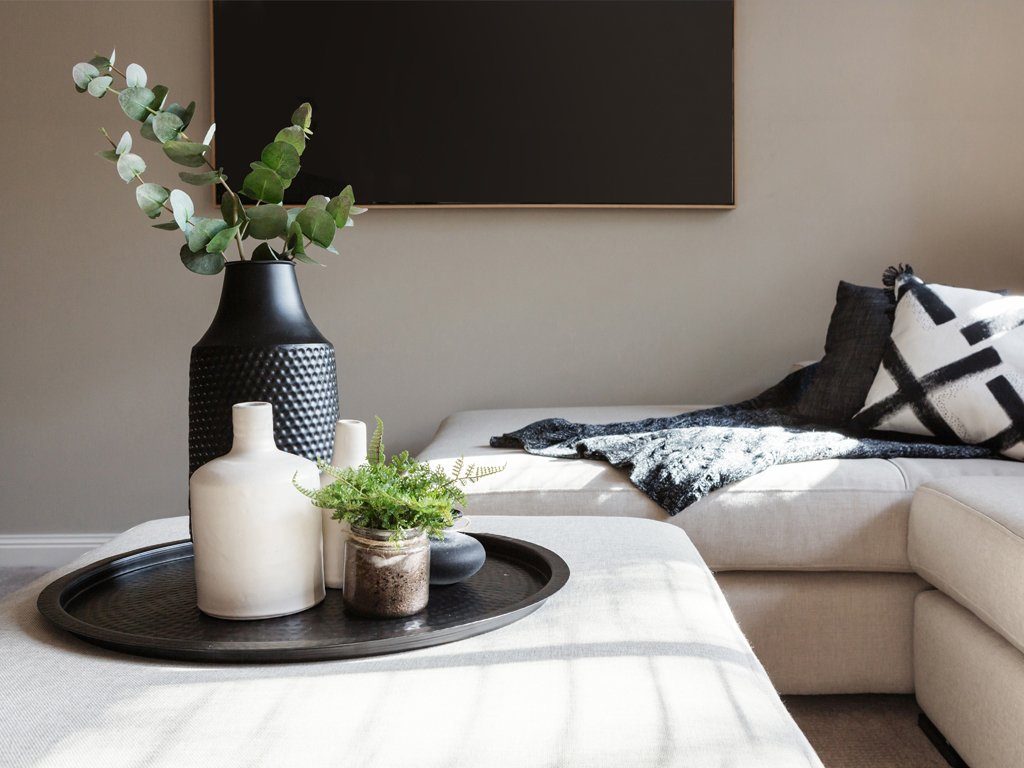 Helles Sofa mit dunkelgrauen Dekoelementen und Flatscreen an der Wand