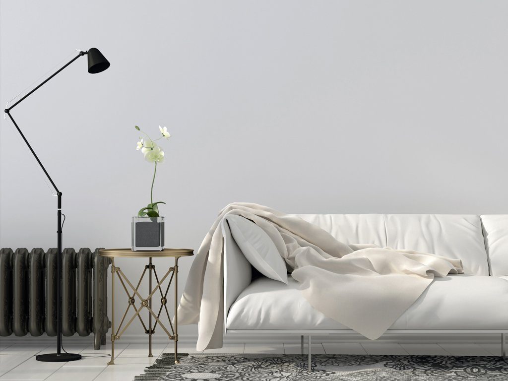 Weißes Sofa vor hellgrauer Wand, schwarzer Rippenheizkörper und schwarz-weißer Teppich