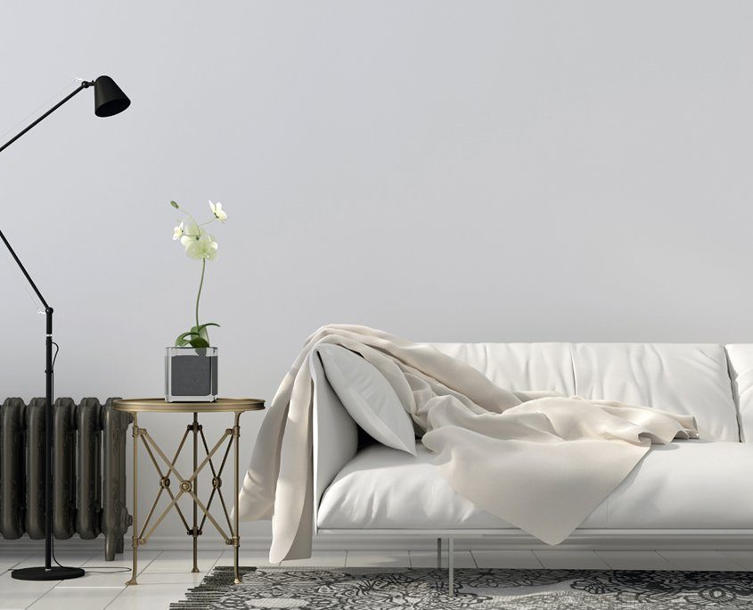 Weißes Sofa vor hellgrauer Wand, schwarzer Rippenheizkörper und schwarz-weißer Teppich