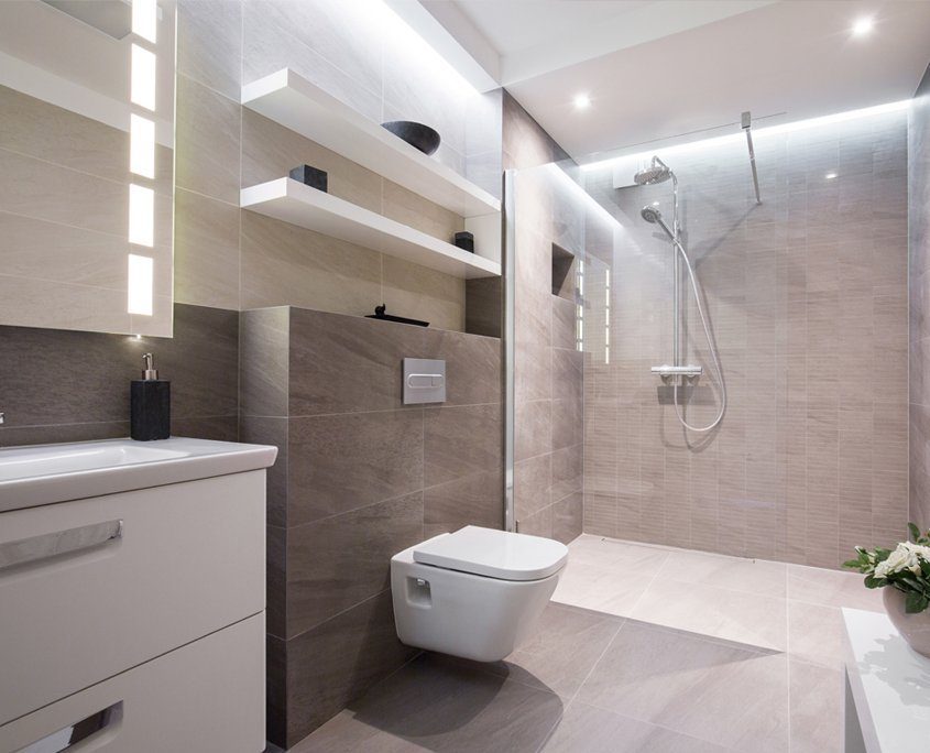 Modernes, grau gefliestes Badezimmer mit weißem Waschbecken und weißer WC Garnitur, sowie einer ebenerdigen Dusche