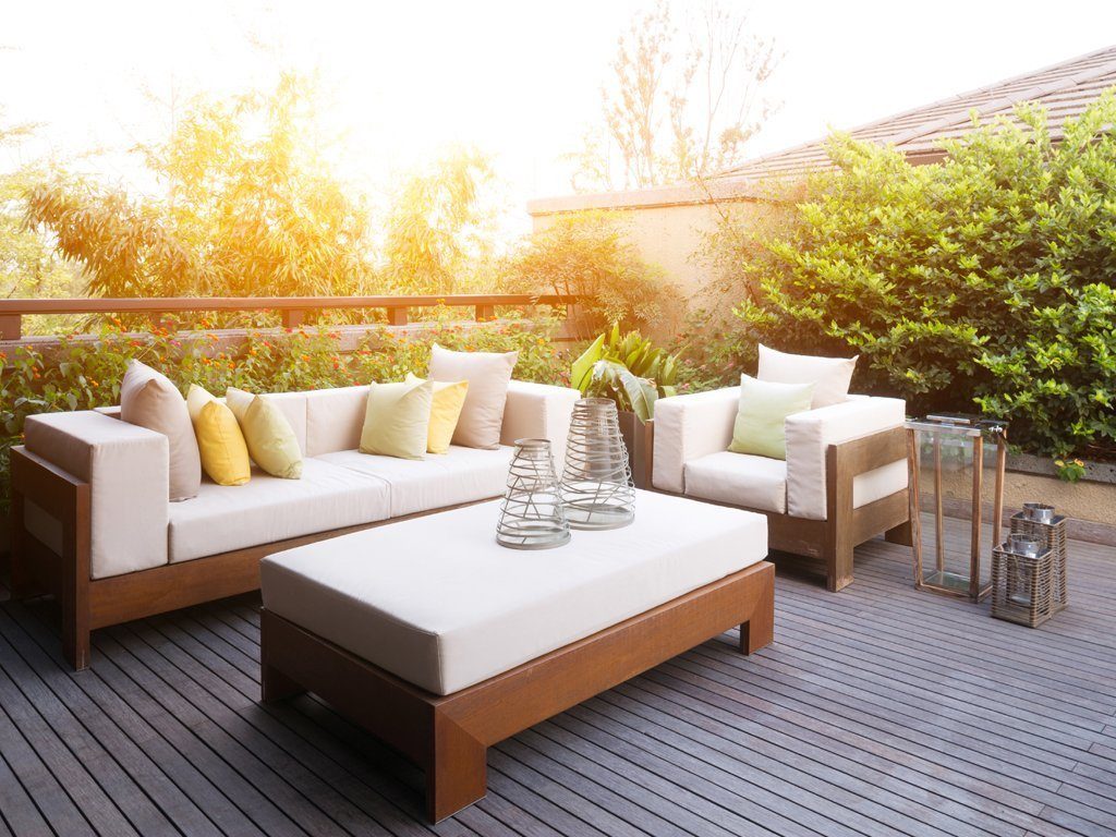 Sonnige Dachterasse mit dunklen Holzdielen und modernen hellen Loungemöbeln