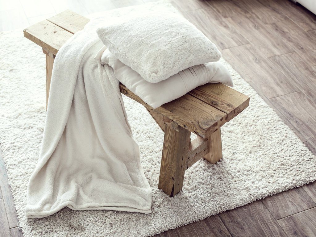 Helle, flauschige Decke und zwei helle Kissen, drapiert auf einer kleinen Holzbank
