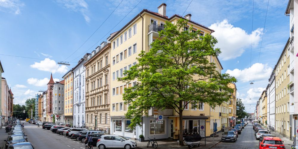 Mehrfamilienhaus Eckgebäude mit gelber Fassade in einer von parkenden Autos gesäumten Stadtstraße