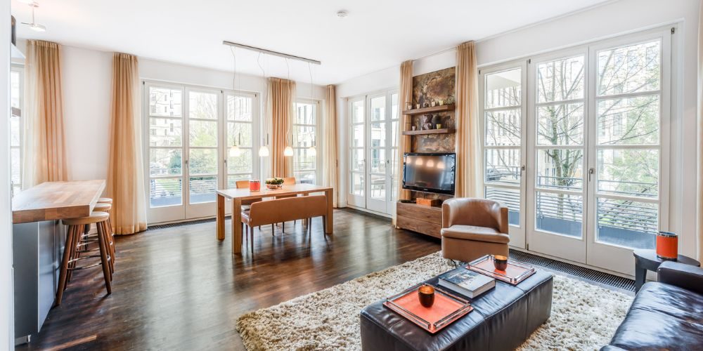 Exklusive Immobilie: Helles und modernes Wohnzimmer einer Stadtwohnung in München mit großen Fenstern, dunklem Holzboden und stilvoller Einrichtung.