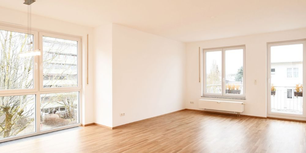 Sonniges, helles Wohnzimmer mit glänzendem Laminat und Ausblicken auf andere Wohngebäude