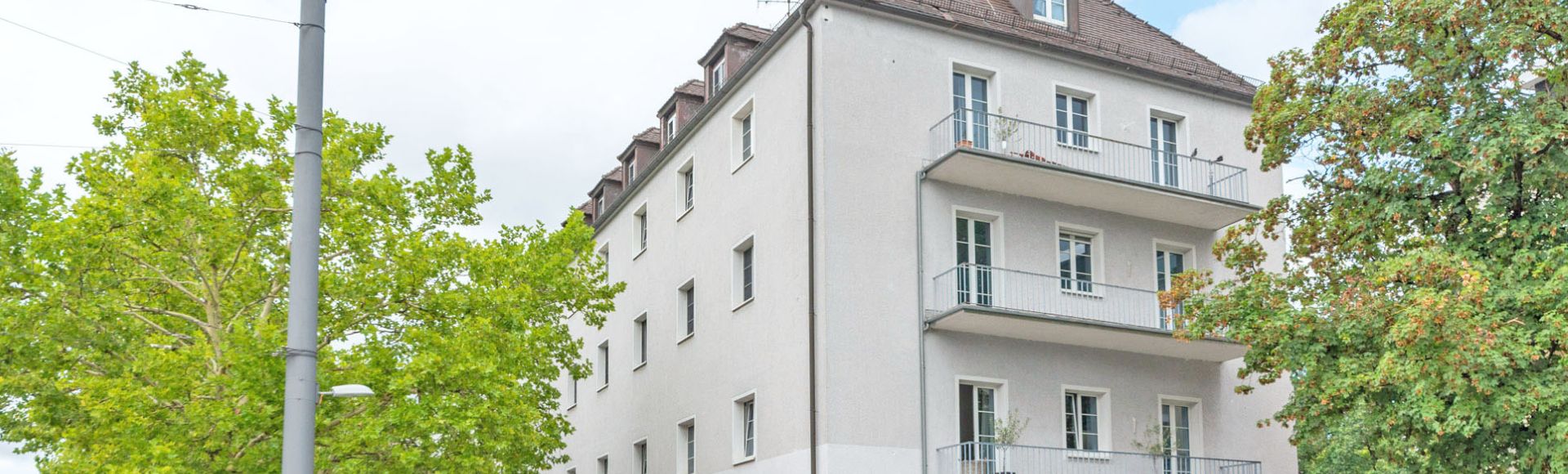 Mehrfamilienhaus in München mit grünen Laubbäumen davor