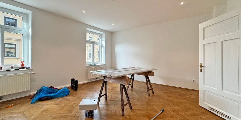 Großzügiger Altbau-Raum in München mit klassischem Fischgrätparkett, hohen Fenstern und großem Tapeziertisch in der Mitte des Raums