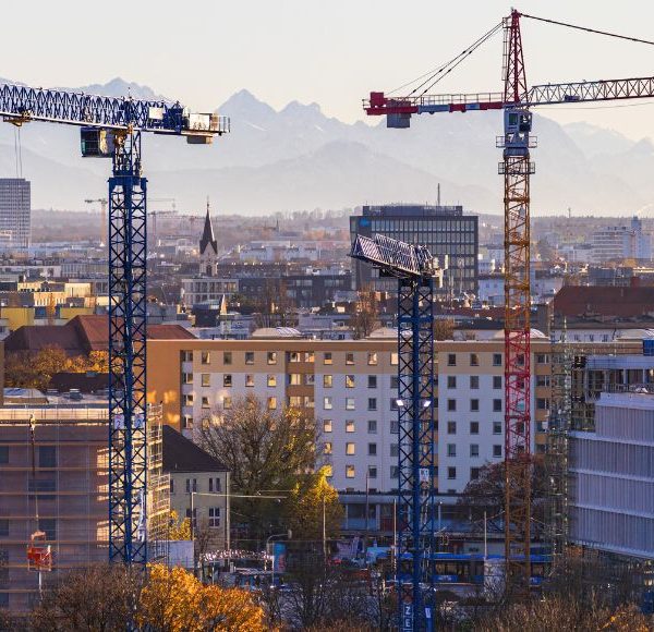 Baustellen und Baukräne vor Münchens Skyline mit Alpenpanorama
