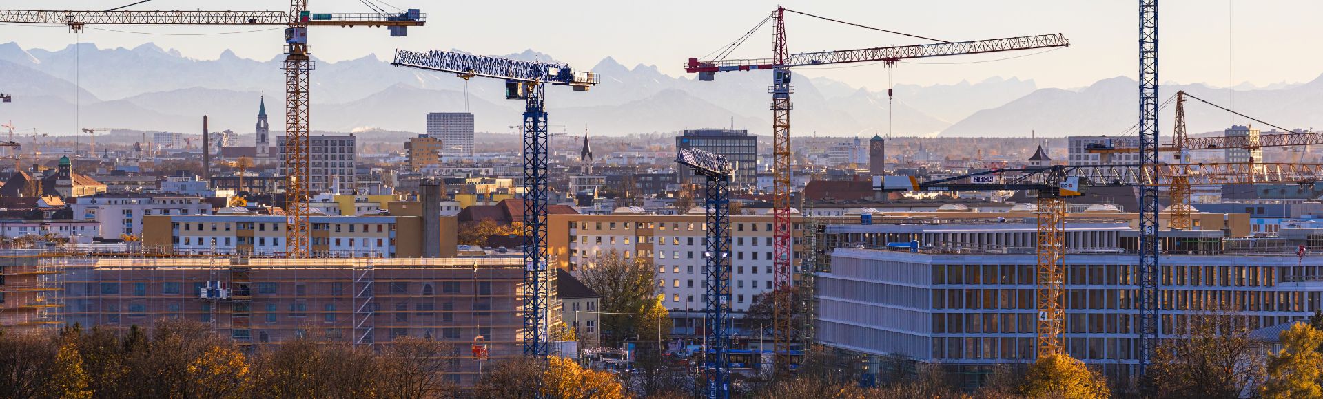 Baustellen und Baukräne vor Münchens Skyline mit Alpenpanorama