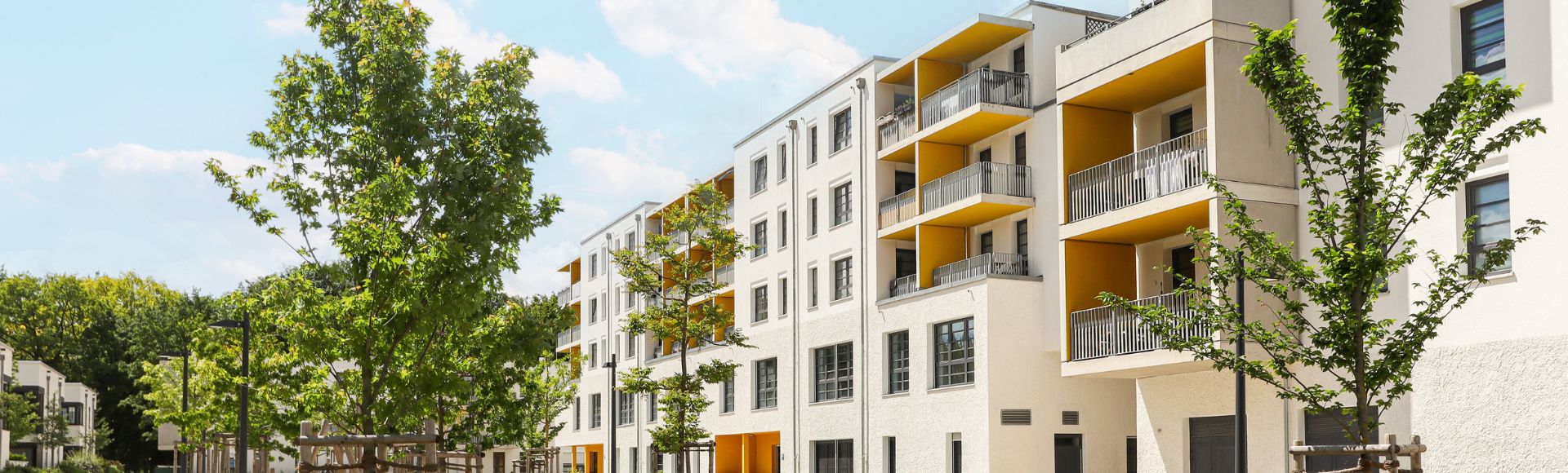 Neubau-Wohnanlage mit Balkonen und Bäumen entlang einer ruhigen Wohnstraße