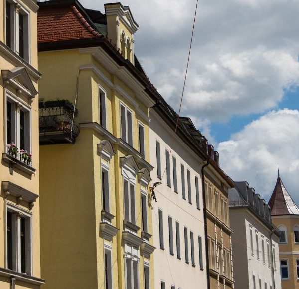 Historische Wohnhäuser mit bunten Fassaden in einer ruhigen Straße in München unter blauem Himmel mit Wolken