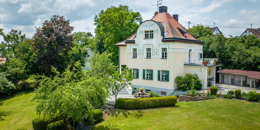 Exklusive helle Jugendstilvilla mit grünen Fensterläden auf einem großen grünen Grundstück