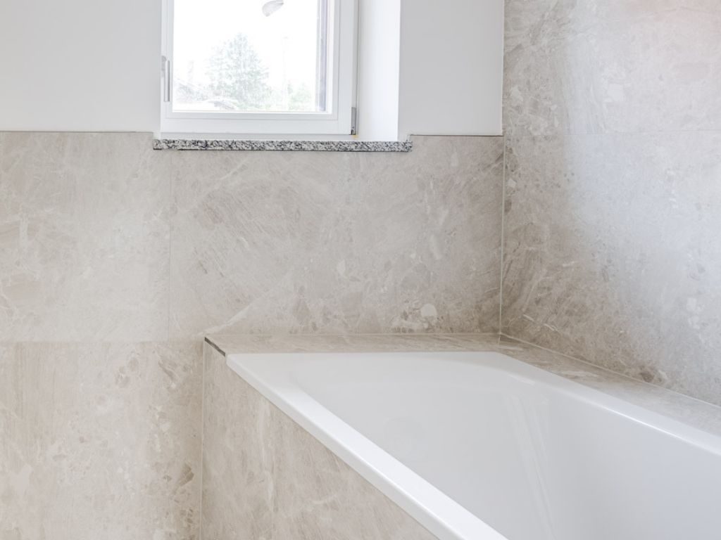 Helles Badezimmer mit großflächiger Natursteinverkleidung und Badewanne in einem Neubau in München