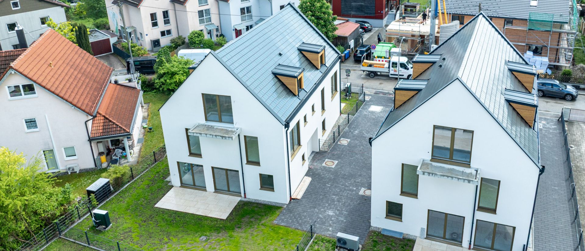Luftaufnahme von modernen Neubau-Doppelhaushälften in München mit Garten und gepflasterter Zufahrt in ruhiger Nachbarschaft