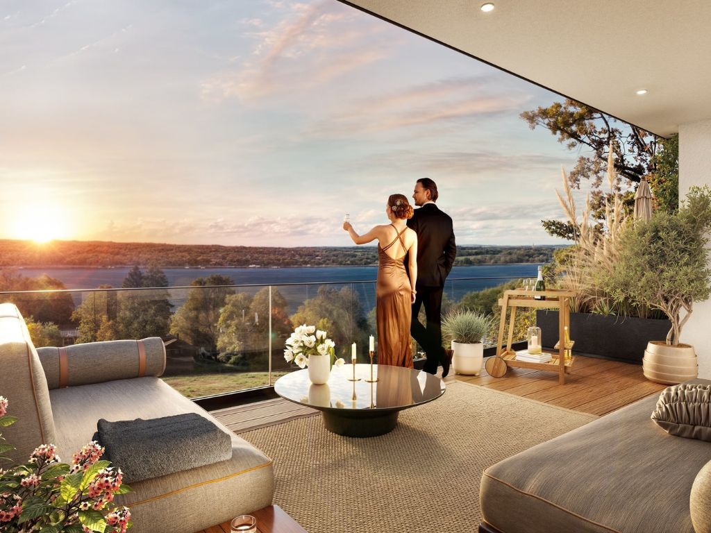 Paar genießt den Panoramablick von einer modernen Penthouse-Terrasse auf einen See nahe München, mit stilvoller Outdoor-Lounge und Glasbrüstung