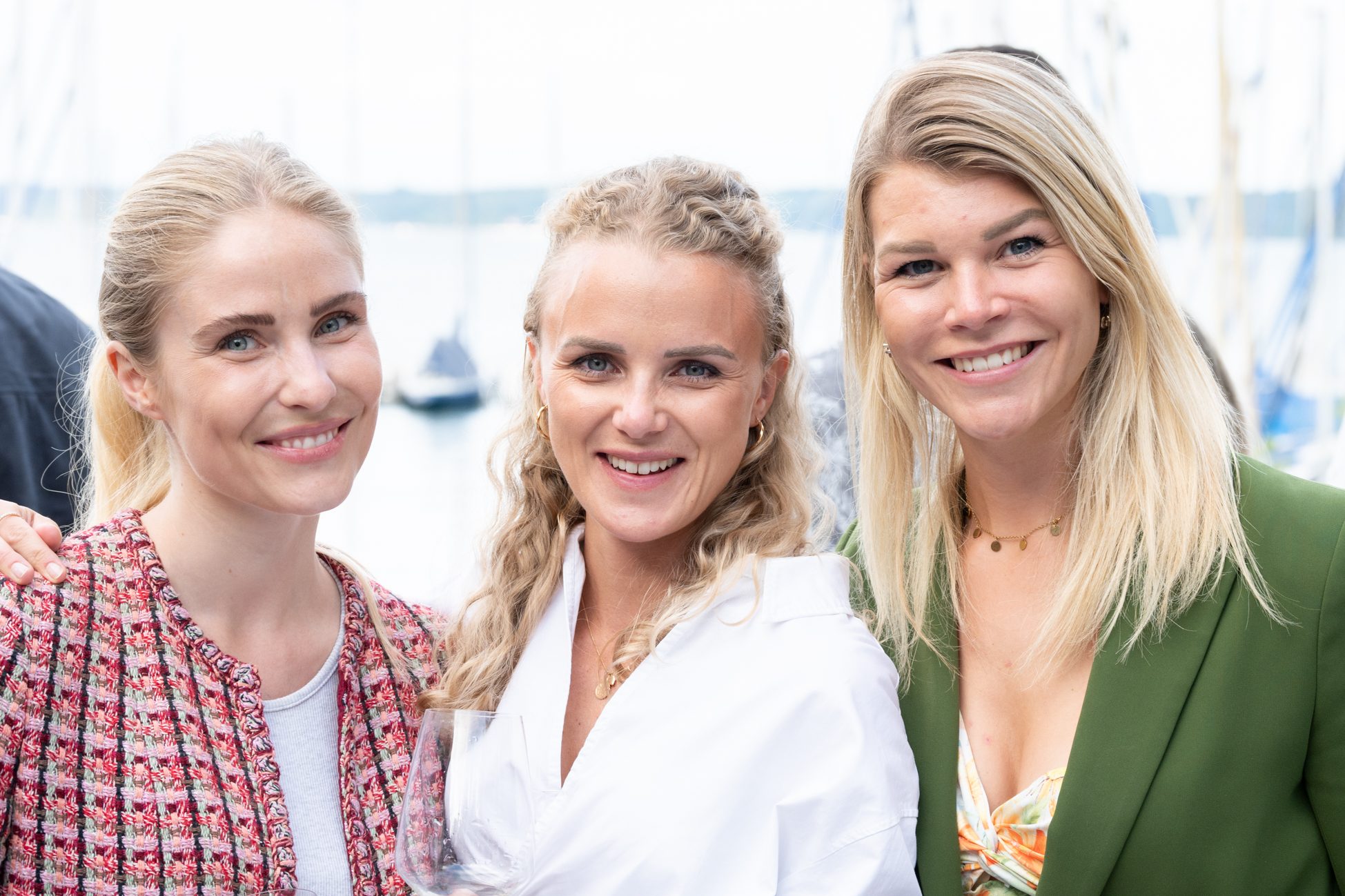 Drei Frauen posieren lächelnd vor Booten und Wasser