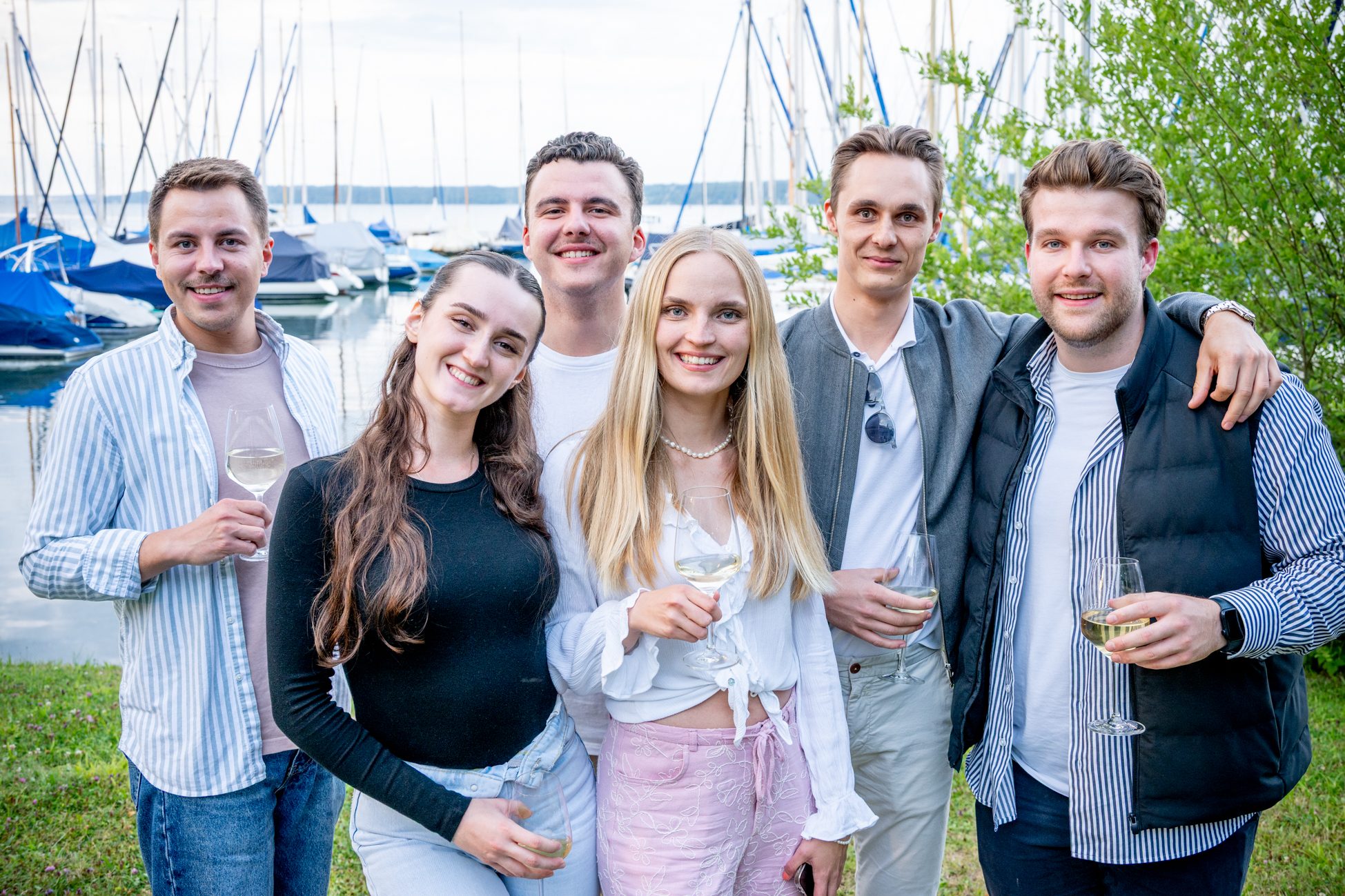 Sechs junge Erwachsene mit Weißweingläsern posieren