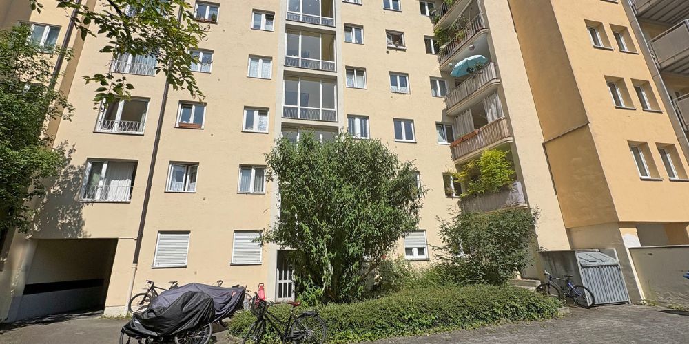 Außenansicht eines gepflegten Mehrfamilienhauses mit Balkonen und begrünter Hoffläche in München