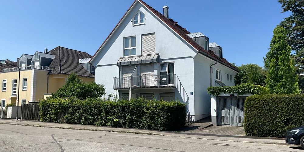 Straßenansicht einer modernen weißen Doppelhaushälfte mit Balkon und gepflegter Begrünung