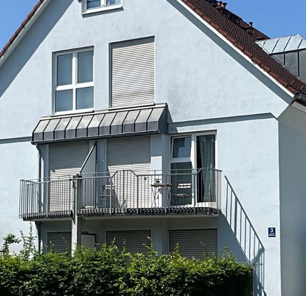 Helles, modernes Mehrfamilienhaus in München mit Balkon, gepflegtem Garten und ruhiger Wohnlage bei blauem Himmel