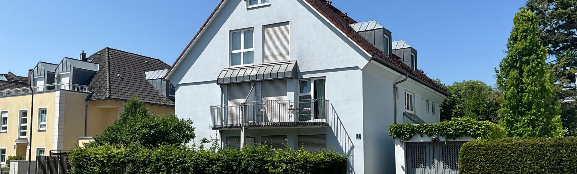 Helles, modernes Mehrfamilienhaus in München mit Balkon, gepflegtem Garten und ruhiger Wohnlage bei blauem Himmel