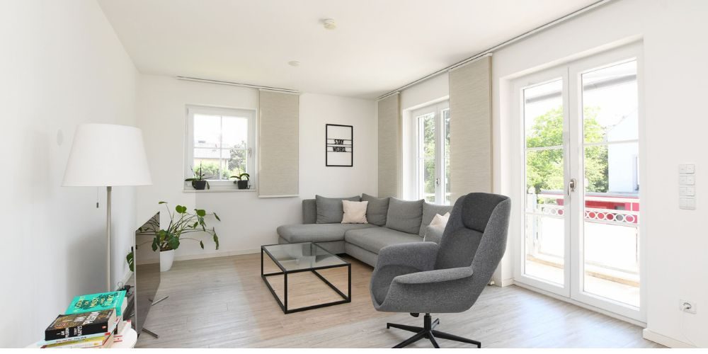 Helles Wohnzimmer mit moderner Einrichtung, grauer Couch und Zugang zum Balkon