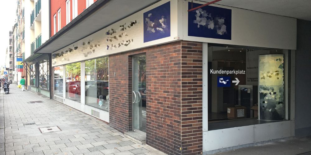 Außenansicht einer vermieteten Gewerbeimmobilie in München mit großem Schaufenster, Eingang und Hinweis auf Kundenparkplatz