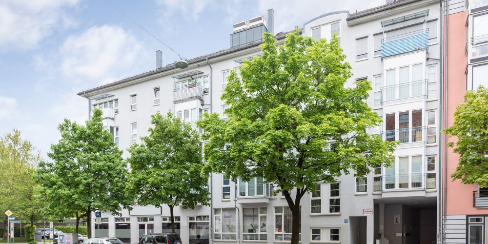 Straßenansicht eines modernen Wohn- und Geschäftshauses in München mit großen Fensterfronten und begrüntem Gehweg