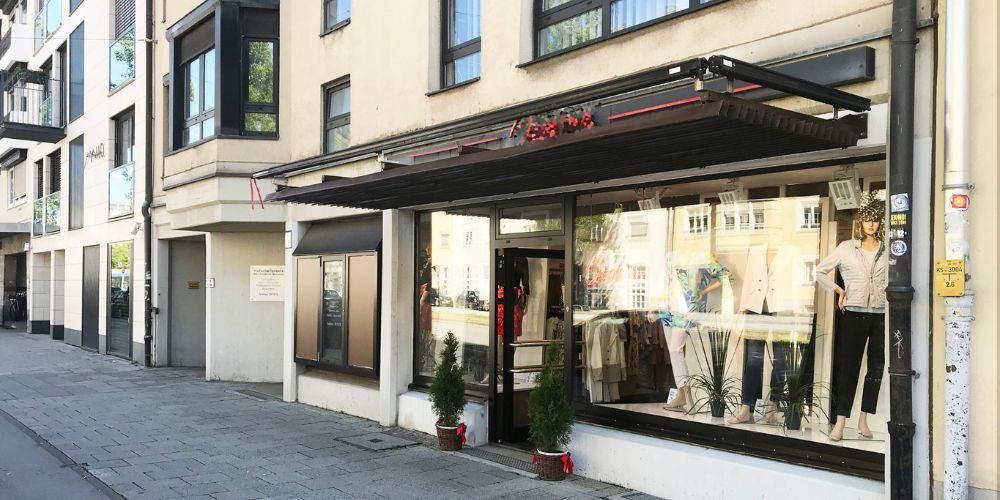 Ansicht eines Schaufensters mit einer Modepuppe und zwei Zuckerfichten links und rechts am Eingang davor