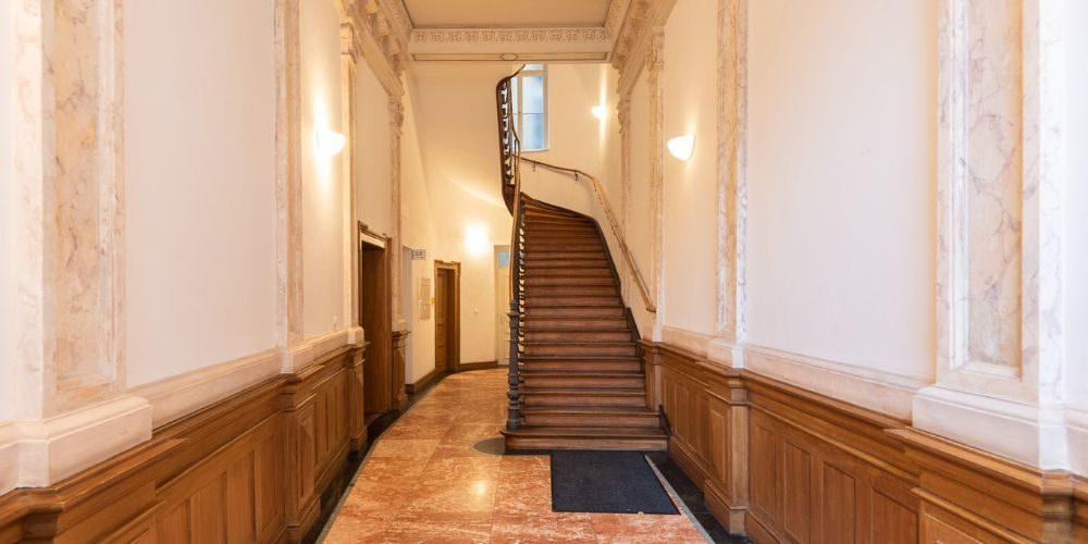 Hochwertiger Eingangsbereich mit Holzvertäfelung, Marmorboden und geschwungener Holztreppe in einer stilvollen Gewerbeeinheit in München, ideal für Kanzlei oder Praxis