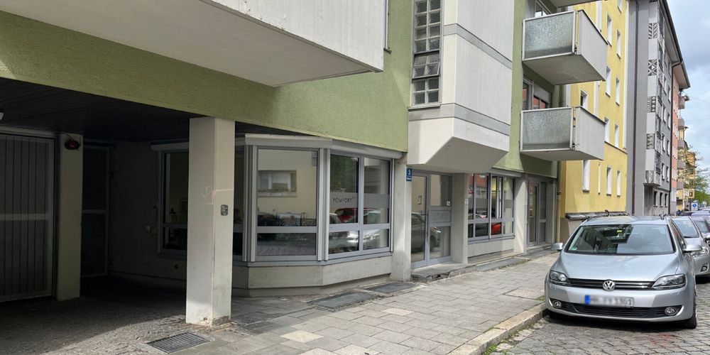 Straßenansicht einer vermieteten Erdgeschoss-Gewerbefläche in München mit großen Fenstern und Wohnbebauung darüber