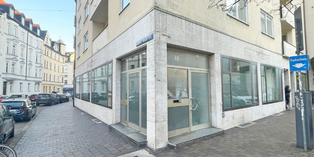 Moderne Gewerbefläche an einer Straßenecke in München mit großen Glasfenstern und heller Natursteinfassade