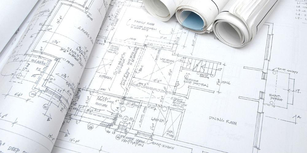 Ausgebreitete Architektenpläne und gerollte Bauzeichnungen einer Gewerbeimmobilie mit Raumaufteilung und Bemaßung