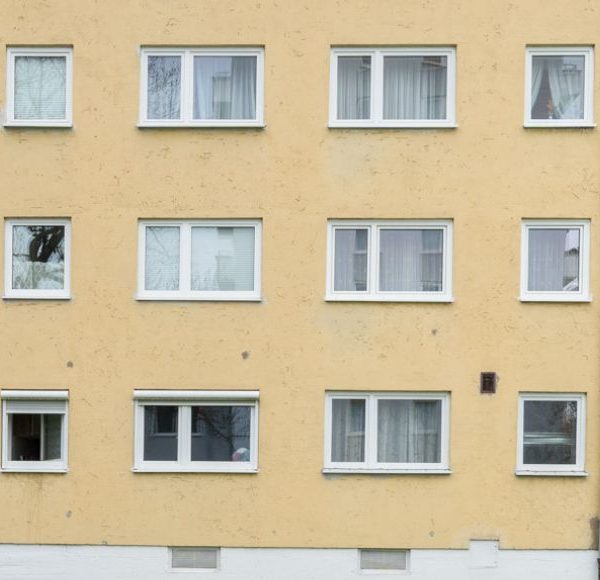 Frontansicht eines gepflegten Mehrfamilienhauses mit Balkonen in München, gelbe Fassade und große Fenster