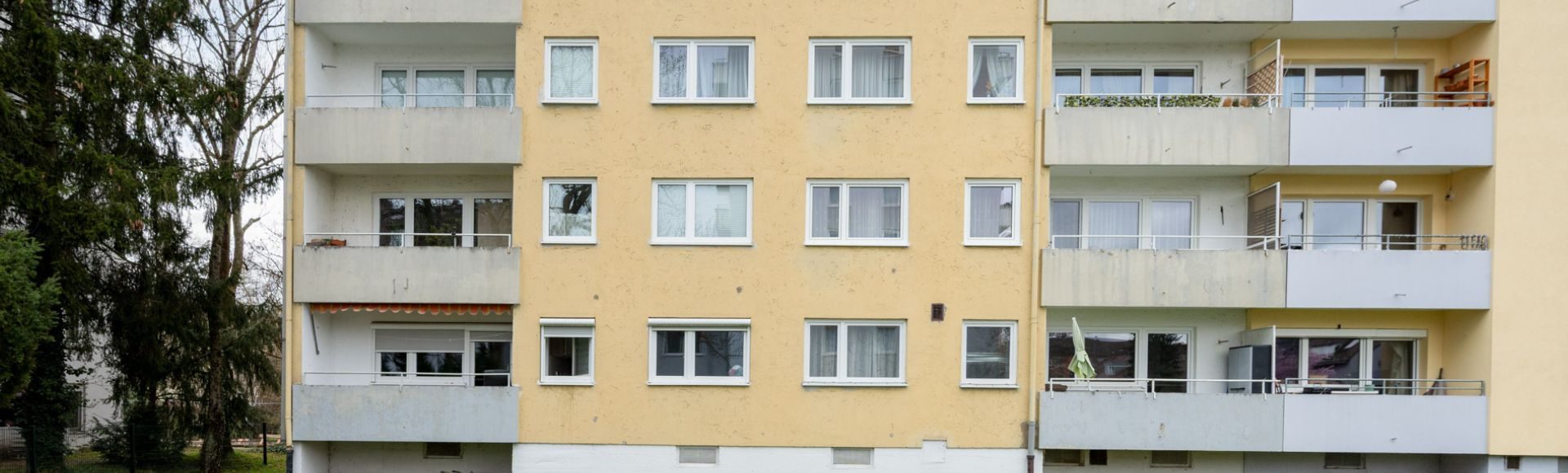 Frontansicht eines gepflegten Mehrfamilienhauses mit Balkonen in München, gelbe Fassade und große Fenster
