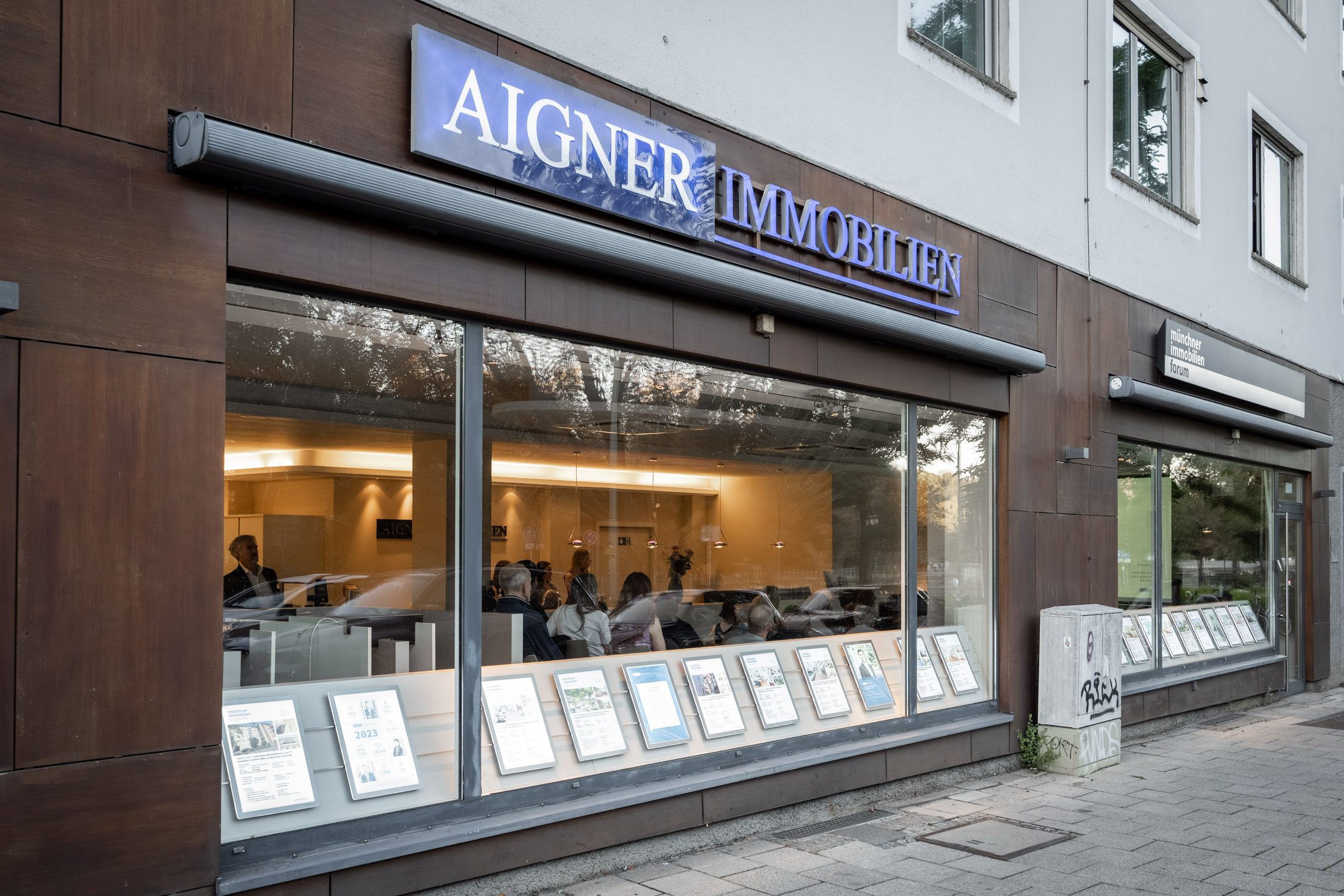 Firmensitz von Aigner Immobilien mit beleuchtetem Schaufenster und Exposés