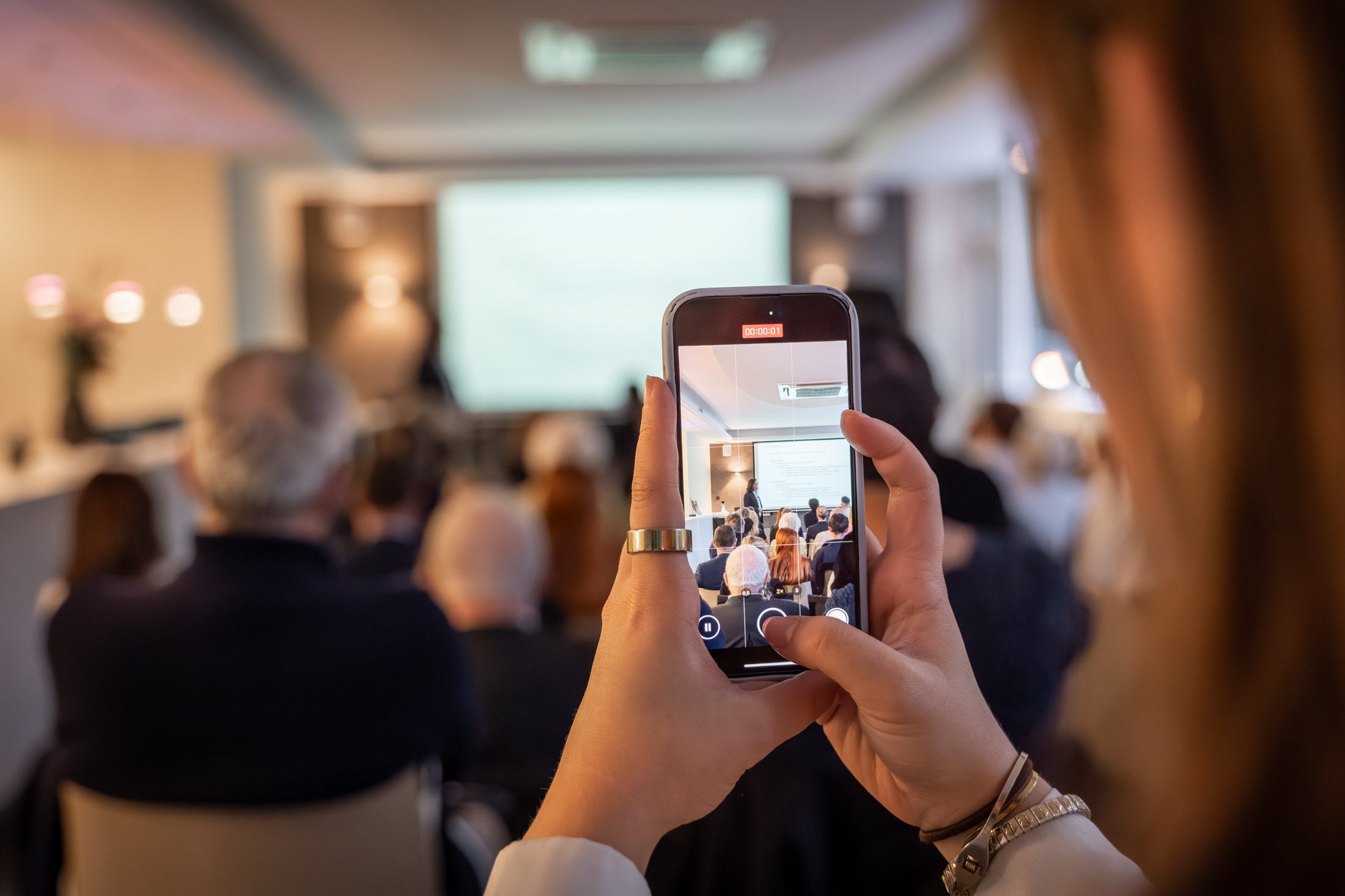 Frau filmt Präsentation eines Immobilienexperten bei Event in München mit dem Smartphone