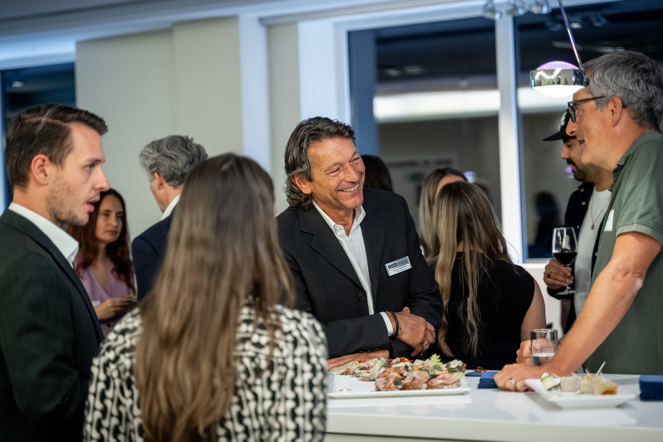 Gäste unterhalten sich an Stehtisch mit Häppchen beim Immobilienevent in München