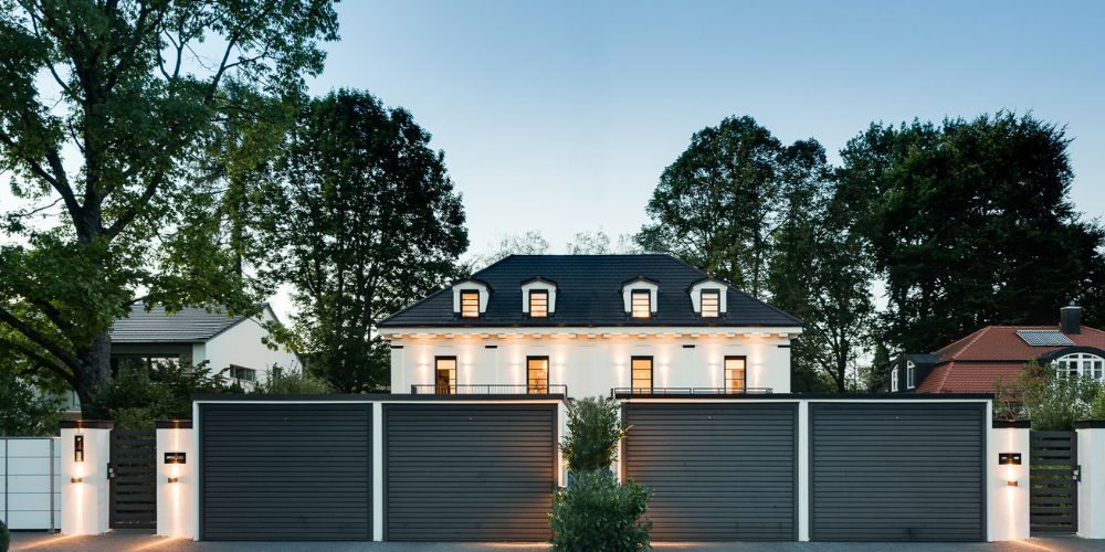 Exklusive Luxusvilla in München (38772) Moderne Stadtvilla in München mit stilvoller Fassade, großem Einfahrtstor und gepflegtem Vorgarten bei Abendbeleuchtung