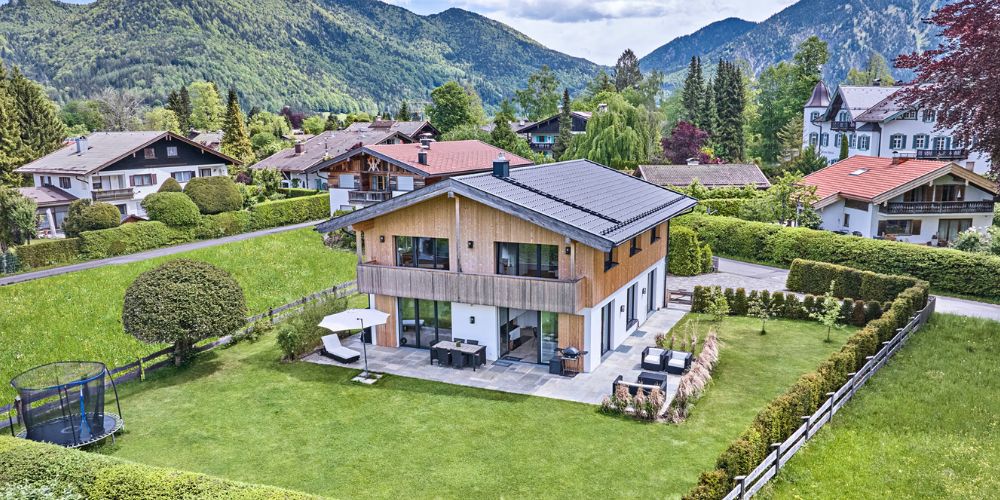 Modernes Einfamilienhaus mit Bergblick (40407) Luftaufnahme eines modernen Einfamilienhauses mit Garten und Terrasse in idyllischer Lage bei München, umgeben von Bergen und traditionellen Häusern