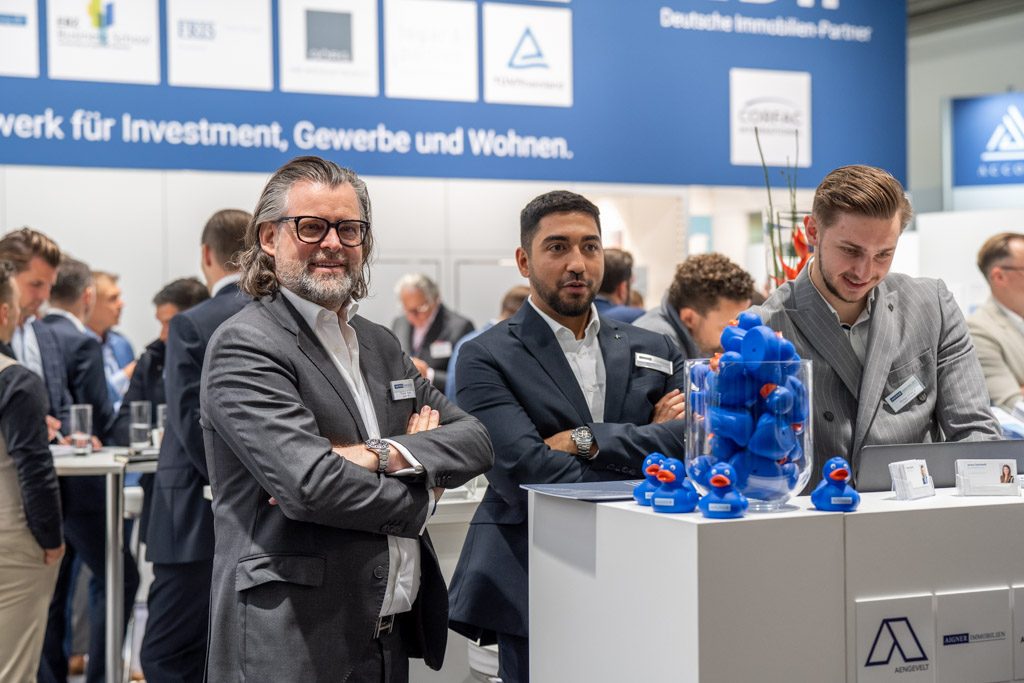 Expo Real 2025: Thomas Aigner mit Investment-Team am Messestand, im Vordergrund Aigner-Badeenten