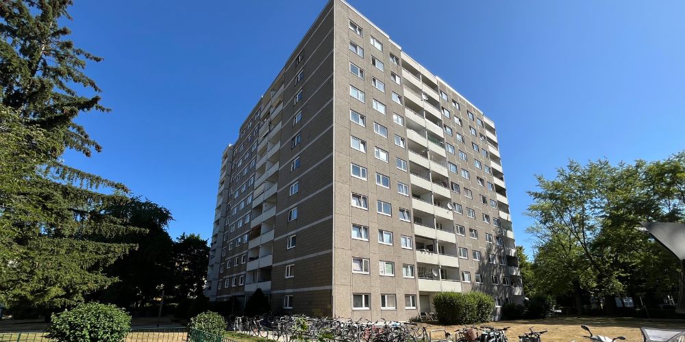 Mehrstöckiges Mehrfamilienhaus in München mit Balkonen, Grünflächen und Fahrradständern an einem sonnigen Tag